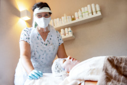 Kosmetikerin Manuela Theurer tragt Maske, Gesichtsschild, Handschuhe und Schürze bei einer Behandlung - Fotoprojekt Nur-so-halb von Stefanie Morlok Fotografin