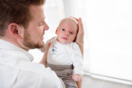 Baby liegt auf der Hand seines Vaters und schaut in die Kamera